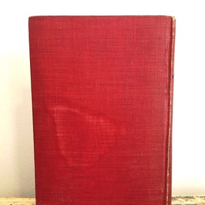 Może przedstawiać: Czerwona książka w twardej oprawie z fakturowaną okładką. Książka leży na drewnianej powierzchni.