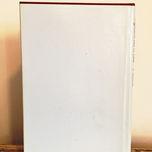May include: A white hardcover book with a red band at the top and a blue band at the bottom. The book has text on the spine.