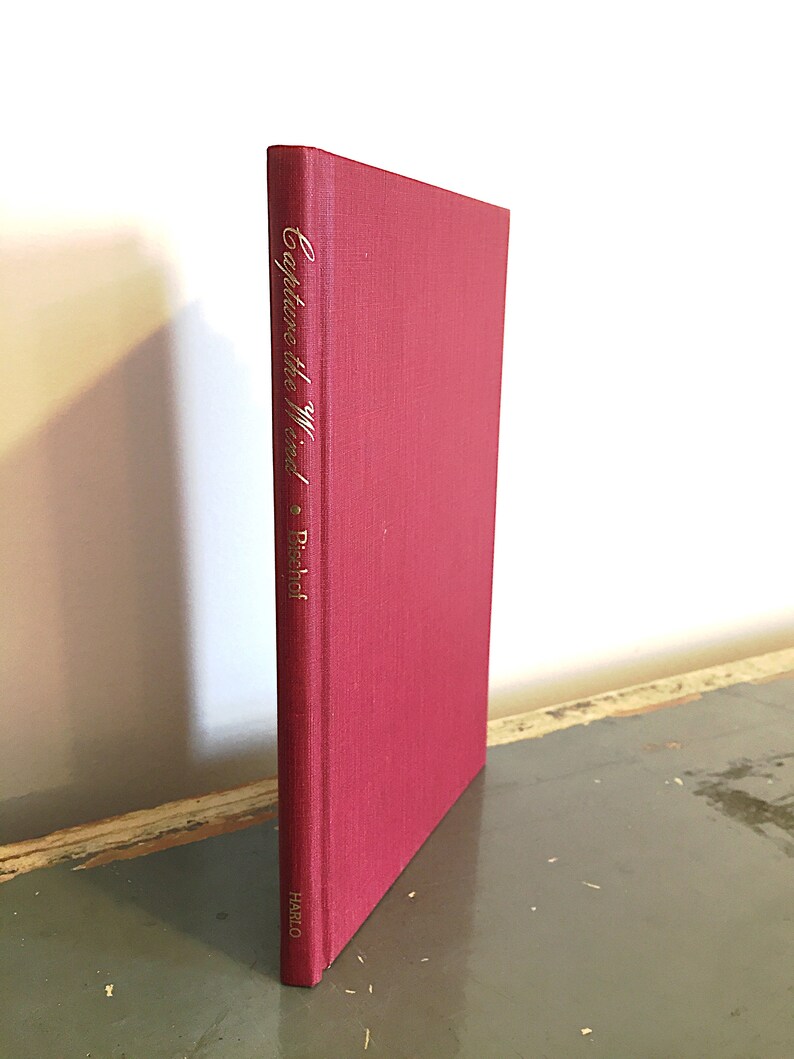 May include: A red hardcover book with the title "Capture the Wind" and the author "P. Bischof" written in gold lettering on the spine. The book is published by Harlo.