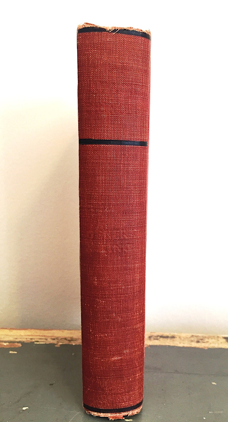 Może przedstawiać: Grzbiet czerwonej książki w twardej oprawie z czarnymi paskami. Książka stoi pionowo na szarej powierzchni.