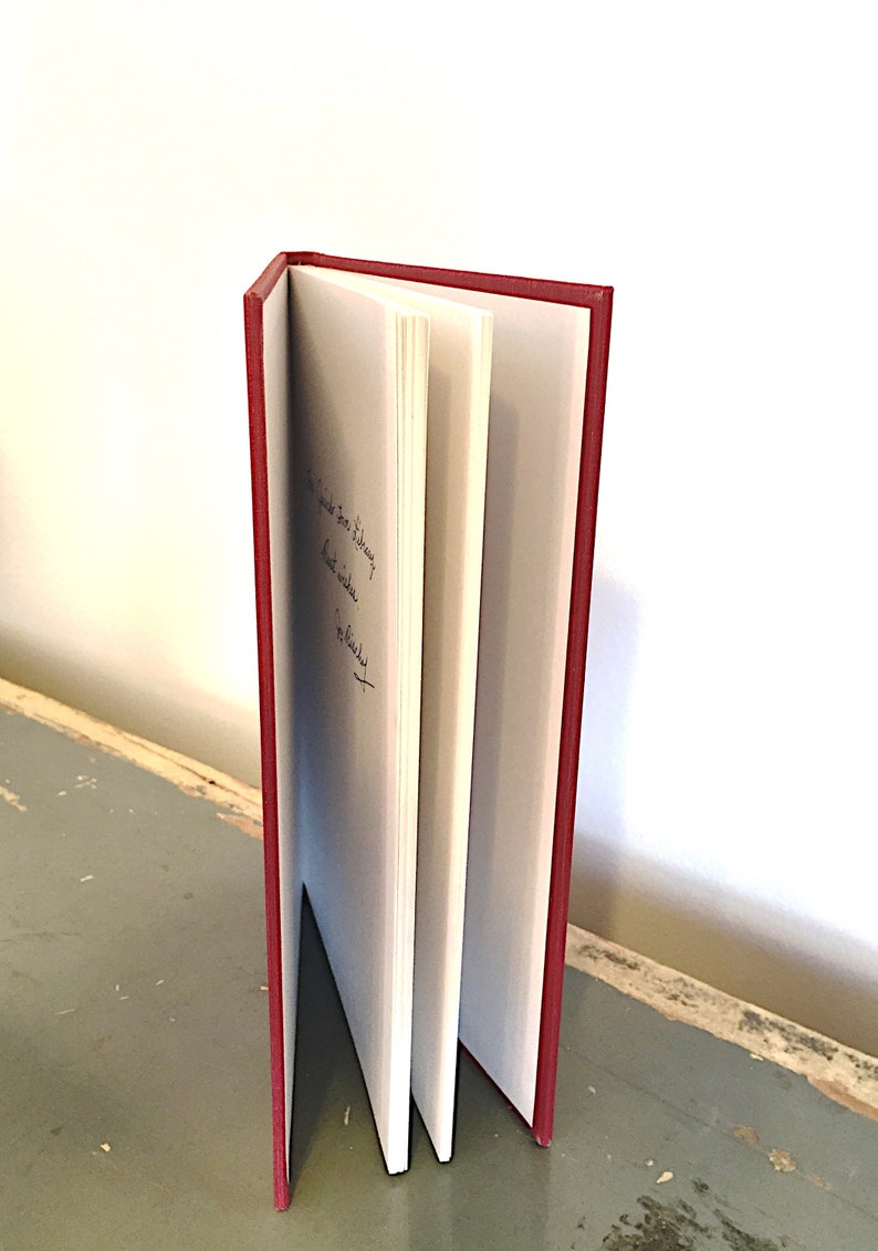 May include: A red hardcover book with a white spine and white pages. The book is open and the pages are fanned out. The book has a handwritten inscription on the inside cover.