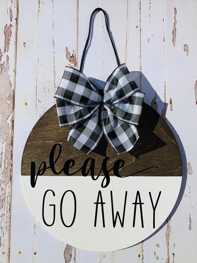 May include: A round wooden sign with a black and white checkered bow. The sign is painted white on the bottom half and brown on the top half. The text "please go away" is written in black on the white half of the sign.