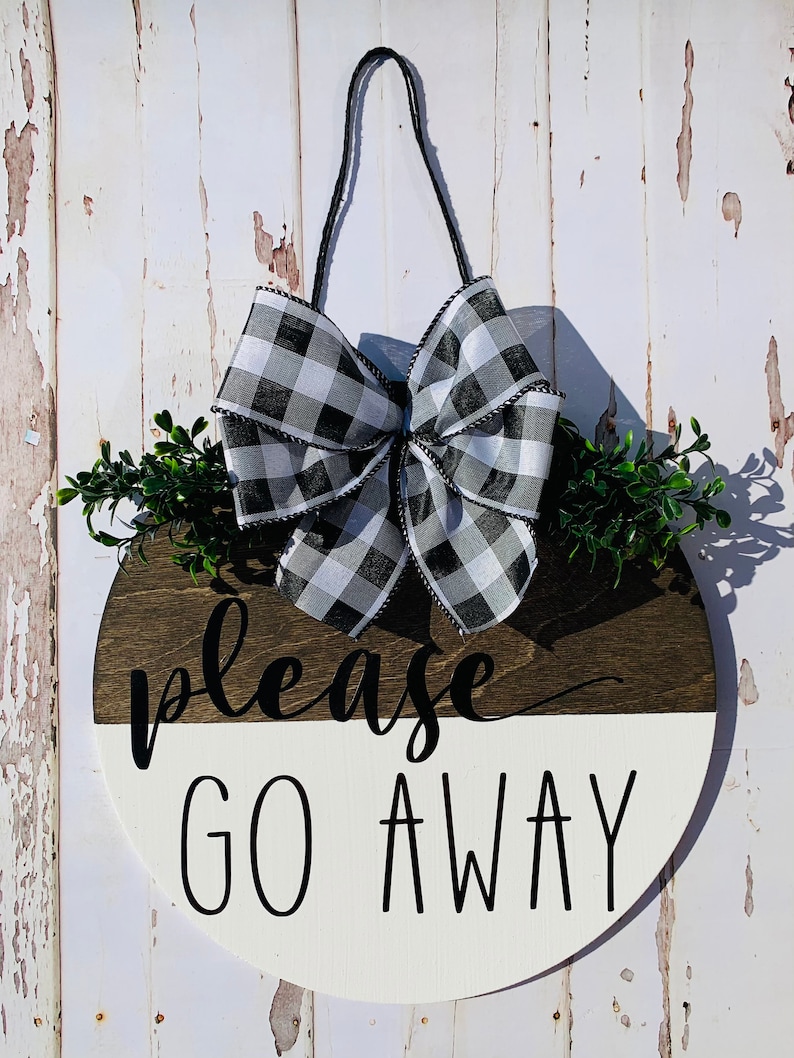 May include: A round wooden door hanger with a black and white checkered bow, green leaves, and the text "please go away" in black lettering.