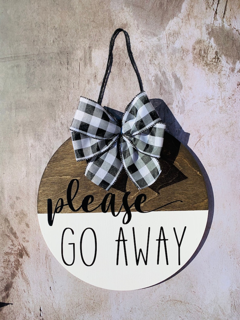 May include: A round wooden sign with a black and white checkered bow. The sign is painted white on the bottom half and brown on the top half. The text "please go away" is written in black on the white half of the sign.