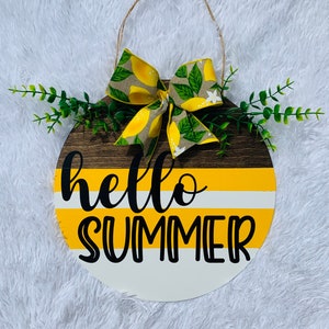 May include: A round wooden sign with a yellow, white, and brown striped design. The sign says "hello summer" in black lettering. A lemon-themed bow is attached to the top of the sign.