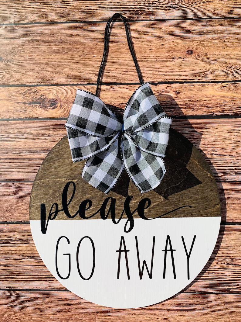 May include: A round wooden sign with a black and white checkered bow. The sign is painted white on the bottom half and brown on the top half. The text "please go away" is written in black on the sign.