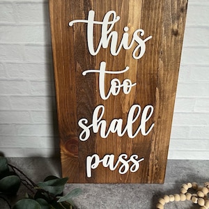 May include: A wooden sign with the text "this too shall pass" in white lettering. The sign has a rustic brown finish and is made of reclaimed wood.