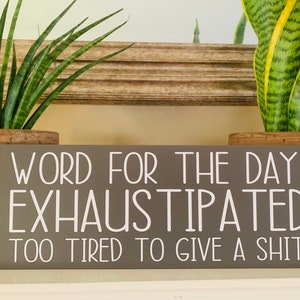 May include: Gray wooden sign with white text that reads "Word for the day: Exhaustipated. Too tired to give a shit."