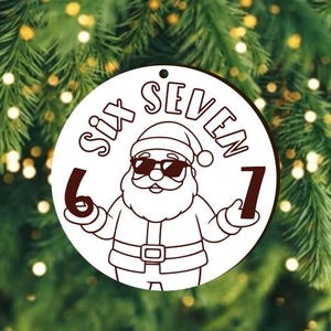 Op de afbeelding: Een ronde, witte kerstversiering met een cartoon kerstman met een zonnebril. De versiering heeft de woorden "SIX SEVEN" en de cijfers 6 en 7. De achtergrond is een wazige afbeelding van een kerstboom.