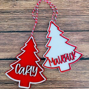 K&ouml;nnte beinhalten: Zwei rote und wei&szlig;e Weihnachtsbaumschmuckst&uuml;cke mit den Namen "Carly" und "Mallory" in wei&szlig; darauf.