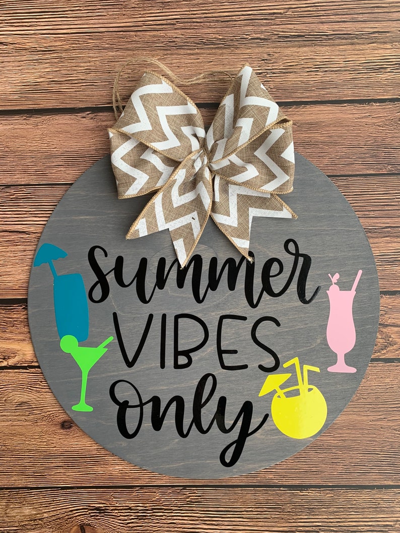 K&ouml;nnte beinhalten: Runder Holzschild mit dem Schriftzug "Summer Vibes Only" in schwarzer Schrift. Es zeigt farbenfrohe Cocktailgrafiken und eine dekorative Schleife mit Zickzackmuster. Das Schild ist grau mit einem Hintergrund aus nat&uuml;rlicher Holzmaserung.