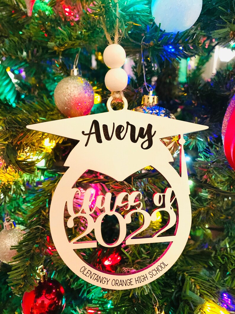 May include: White wooden ornament with a graduation cap design. The ornament says "Avery Class of 2023 Olentangy Orange High School".