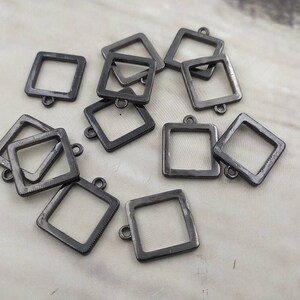 Puede incluir: Un grupo de diez marcos cuadrados de metal negro con un bucle en la parte superior. Los marcos son todos del mismo tamaño y forma, y están dispuestos en un patrón aleatorio.