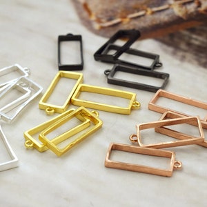 May include: An assortment of rectangular metal jewelry findings in various colors, including silver, gold, black, and copper. Each frame has small loops on the short ends for attaching to other components. The findings are scattered on a light-colored surface.
