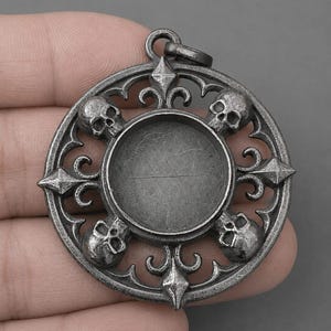 以下が含まれることがあります： 中央に円形のくぼみがある円形の金属製ペンダント。フレームには4つの小さな頭蓋骨と4つの尖ったフルール・ド・リス風の装飾が施されており、中心の周りに交互に配置されています。