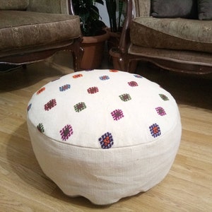 May include: A white round ottoman with a colorful geometric pattern. The ottoman is made of fabric and has a thick, padded cushion.