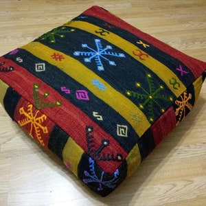 May include: A colorful square floor cushion with a geometric pattern in shades of red, yellow, black, and green. The cushion is made of woven fabric and has a tufted design.