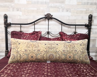 May include: A decorative bed with a black metal headboard and a burgundy and gold patterned bedspread. A large patterned bolster pillow is on top of the bedspread. The headboard has a decorative design at the top.