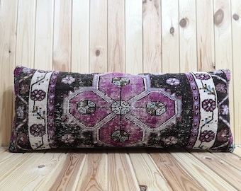May include: A long, rectangular pillow with a pink, black, and white patterned fabric. The pillow is made from a woven fabric with a traditional design.