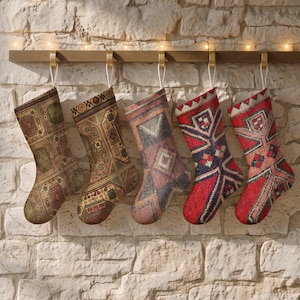 Könnte beinhalten: Fünf Weihnachtsstrümpfe hängen an einer Holzleiste, jeder mit einem eigenen Webmuster. Die Designs zeigen komplexe geometrische und florale Motive in Braun-, Beige-, Blau-, Rot- und Cremetönen, ausgestattet mit weißen Aufhängeschlaufen.
