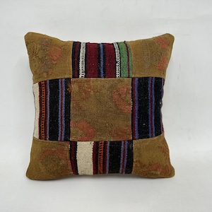 May include: A square throw pillow with a patchwork design. The pillow is made of different colored fabrics, including brown, red, blue, and green. The pillow has a fringe border.