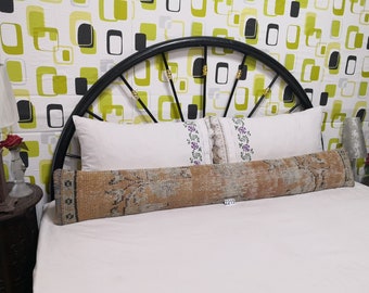 May include: A long, rectangular, brown and beige patterned pillow with a white tag that says "2215" is placed on a white bed with white pillowcases. The bed has a black metal headboard with a circular design.