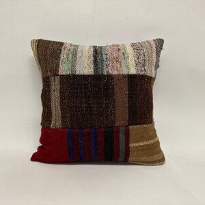 May include: A patchwork pillow cover with a variety of colors and textures, including brown, red, beige, and blue. The pillow cover is made of woven fabric and has a rectangular shape.