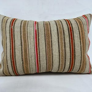 Puede incluir: Una almohada de rayas con fondo beige y rayas rojas, marrones y rosas.