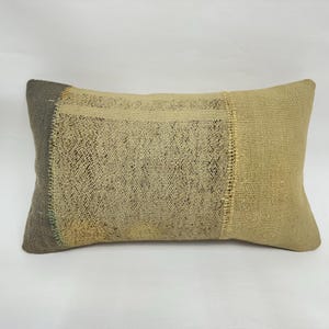May include: Rectangular cushion with a patchwork design. The cushion features beige, tan, and grey tones. The fabric appears woven, with visible texture and stitching details. The cushion is designed for home decor and measures approximately 40cm x 60cm.