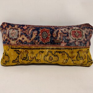 May include: A rectangular pillow with a yellow, blue, red, and white patterned fabric. The pillow is made from a woven fabric with a vintage look.