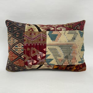 May include: Rectangular cushion with a patchwork design. The cushion displays geometric patterns in burgundy, teal, beige, and brown. Likely made of woven fabric, it adds texture and colour to a room. Measurements are in centimetres.