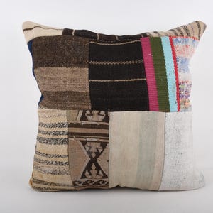 May include: Square patchwork pillow with a variety of textures and colors. The pillow features squares of brown, black, beige, and white fabrics, with accents of blue, pink, and green. The pillow is a decorative item for a bed or sofa.
