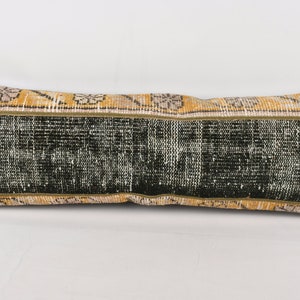 May include: A long, rectangular pillow with a black and yellow patterned fabric. The pillow has a dark green center with a yellow and white border.