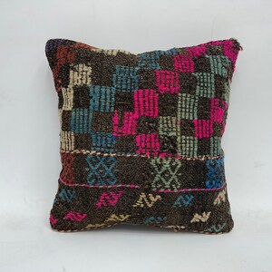 May include: A colorful, handwoven pillow cover with a geometric pattern in shades of pink, blue, green, and brown. The pillow cover is made of a thick, textured fabric and has a fringe border.