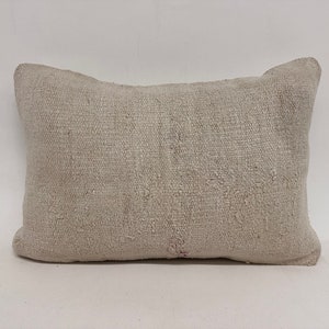 Puede incluir: Una almohada rectangular blanca con un tejido tejido texturizado. La almohada está hecha de un material natural suave y tiene un aspecto ligeramente desgastado.