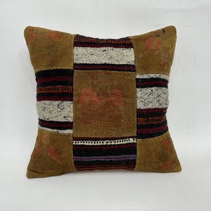 May include: A patchwork pillow with a brown, red, black, and white geometric pattern. The pillow is made of woven fabric and has a square shape.