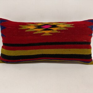 May include: A red, green, black, and blue patterned throw pillow with a geometric design. The pillow is made of woven fabric and has a rectangular shape.