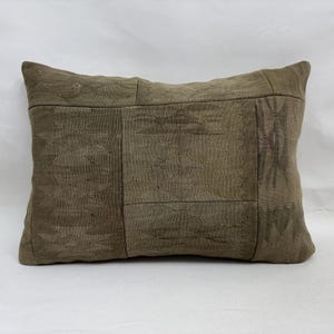 May include: A rectangular pillow with a patchwork design in shades of brown and tan. The pillow has a textured appearance, with visible stitching and varying patterns across the surface. The pillow is designed for decorative use.