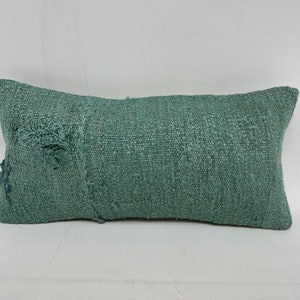 Peut inclure: Un coussin rectangulaire doux et vert en tissu tissé texturé. Le coussin a un bord effiloché et est fait d'un matériau naturel.