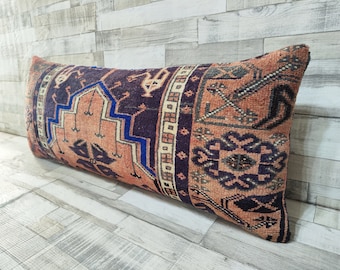 May include: A long, rectangular pillow with a colorful, intricate pattern. The pillow is made of a woven fabric with a variety of colors, including red, orange, blue, and black. The pillow is lying on a wooden floor.