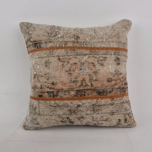 May include: A square throw pillow with a beige background and a brown and black geometric pattern. The pillow has two brown stripes across the center.