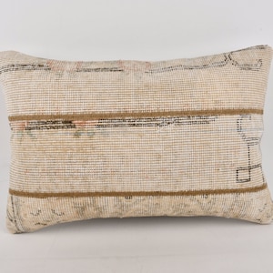 Puede incluir: Una almohada rectangular de color beige con rayas marrones. La almohada tiene una textura tejida y un patrón sutil.