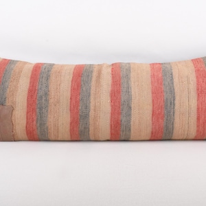 May include: Rectangular pillow with vertical stripes in red, gray, and beige. A brown leather patch is sewn on one end. The pillow is a decorative item for a bed or sofa.