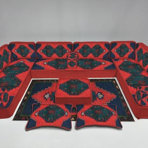 May include: A modular red sofa set with a geometric pattern in teal and navy blue. The set includes a large sectional, ottoman, rug, and two throw pillows. The design features a repeating diamond motif.