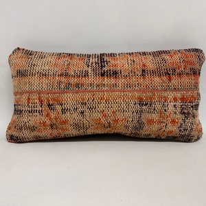 Op de afbeelding: Een rechthoekig kussen met een geweven patroon in beige, oranje en zwarte tinten. Het kussen heeft een subtiele glans en een licht verweerde uitstraling.
