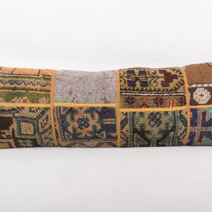 May include: Rectangular decorative pillow with a patchwork design. The pillow features various rectangular patches in shades of brown, blue, green, and orange, with intricate patterns. The pillow is approximately 30 inches long.