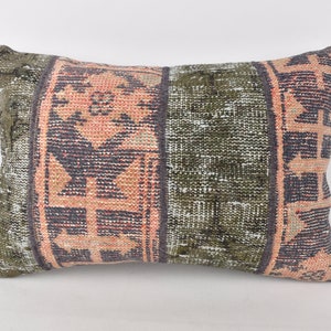 May include: A rectangular pillow with a patterned design. The pillow is made of a woven fabric with a green, pink, and black color scheme. The pattern is geometric and includes a variety of shapes and lines.