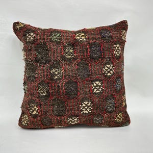 May include: Square decorative pillow with a woven geometric pattern in shades of brown, red, and cream. The pillow has a textured surface and a traditional design, suitable for home decor.