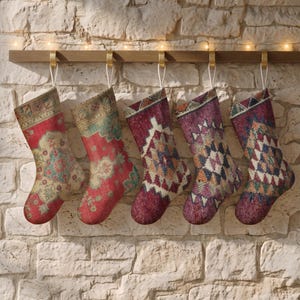 Könnte beinhalten: Fünf Weihnachtsstrümpfe hängen an einer Holzleiste, jeder mit einem einzigartigen Webmuster. Die ersten beiden Strümpfe zeigen komplexe florale Motive in Rot, Creme und Türkis, während die restlichen drei geometrische Rautenmuster in den Farben Dunkelrot, Violett, Blau und Grün aufweisen.