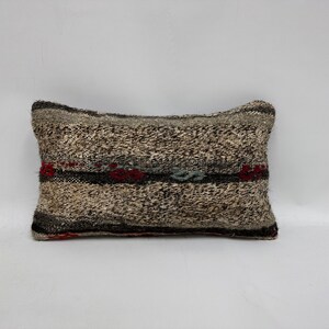 May include: A rectangular pillow with a woven pattern in shades of gray, white, and red. The pillow has a slightly textured surface.